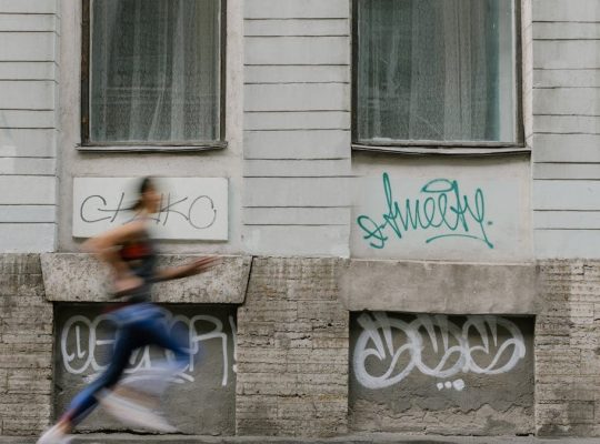 Blurred motion of a woman running past a graffiti-covered urban wall. Captures dynamic energy.