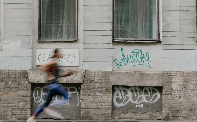 Blurred motion of a woman running past a graffiti-covered urban wall. Captures dynamic energy.